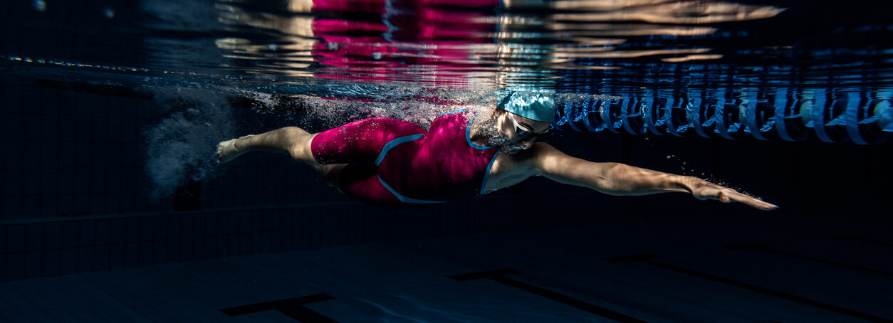 Underwater shooting. One female swimmer training at pool, indoors. Underwater view of swimming movements details.