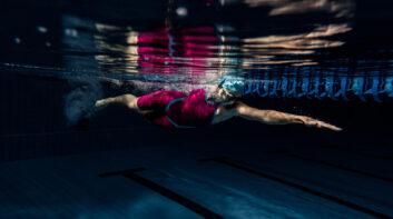 Underwater shooting. One female swimmer training at pool, indoors. Underwater view of swimming movements details.