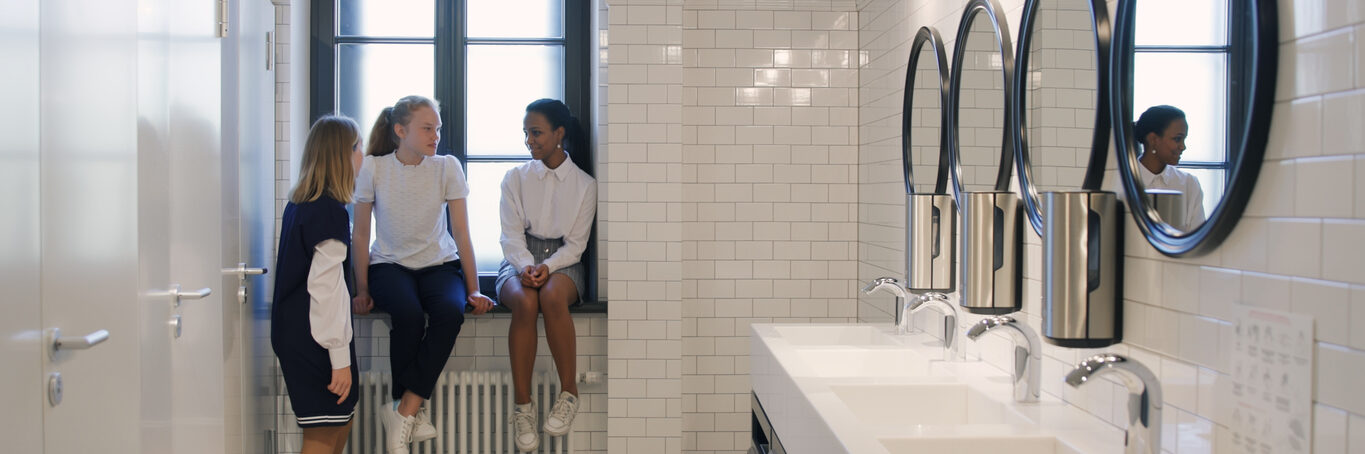 Multiethnic teen girlfriends chat in school bathroom during break